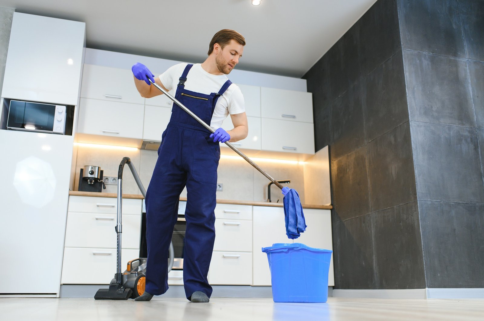 Man as a professional cleaner in blue uniform washing floor